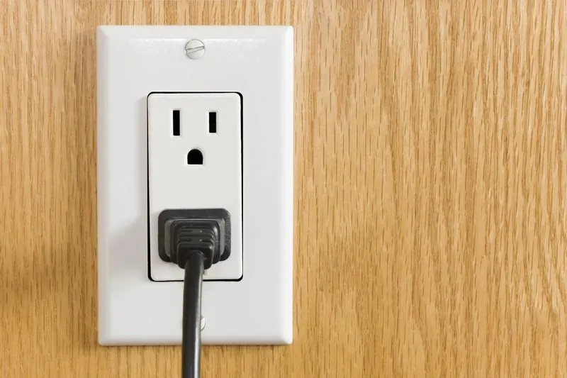white duplex outlet with a black plug inserted, on a wood-grain wall