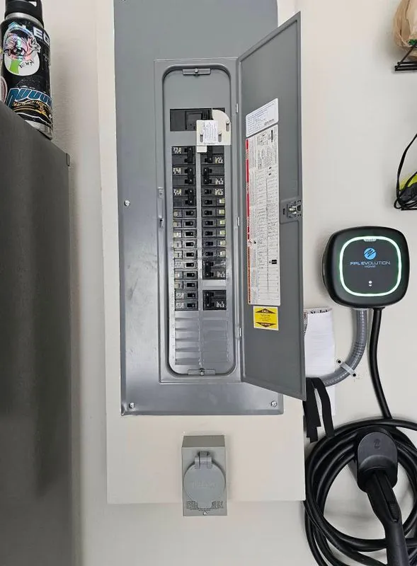 grey residential breaker panel with a wall-mounted EV charger and cable beside it