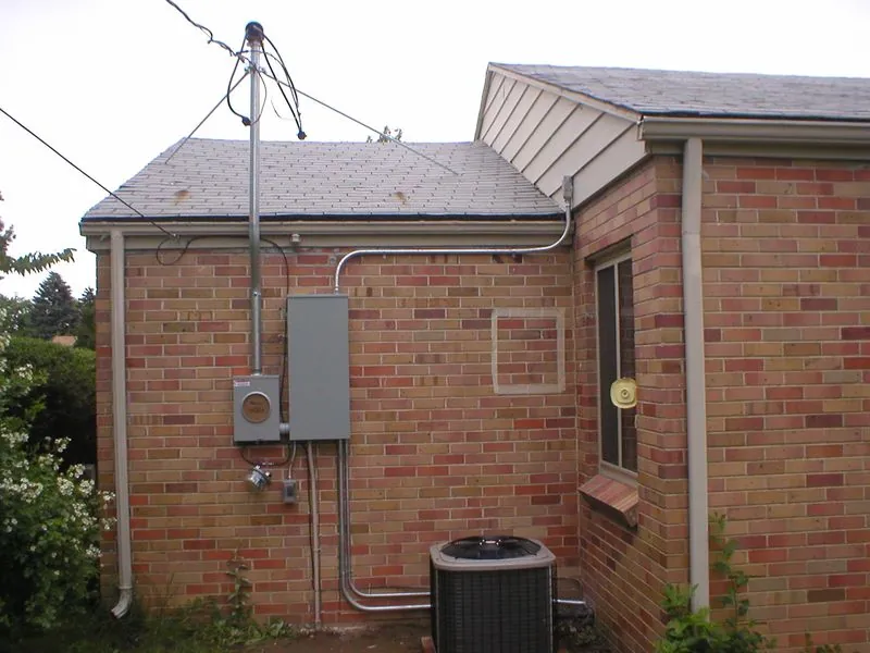 Exterior brick wall with electric meter, panel, conduit and AC condenser