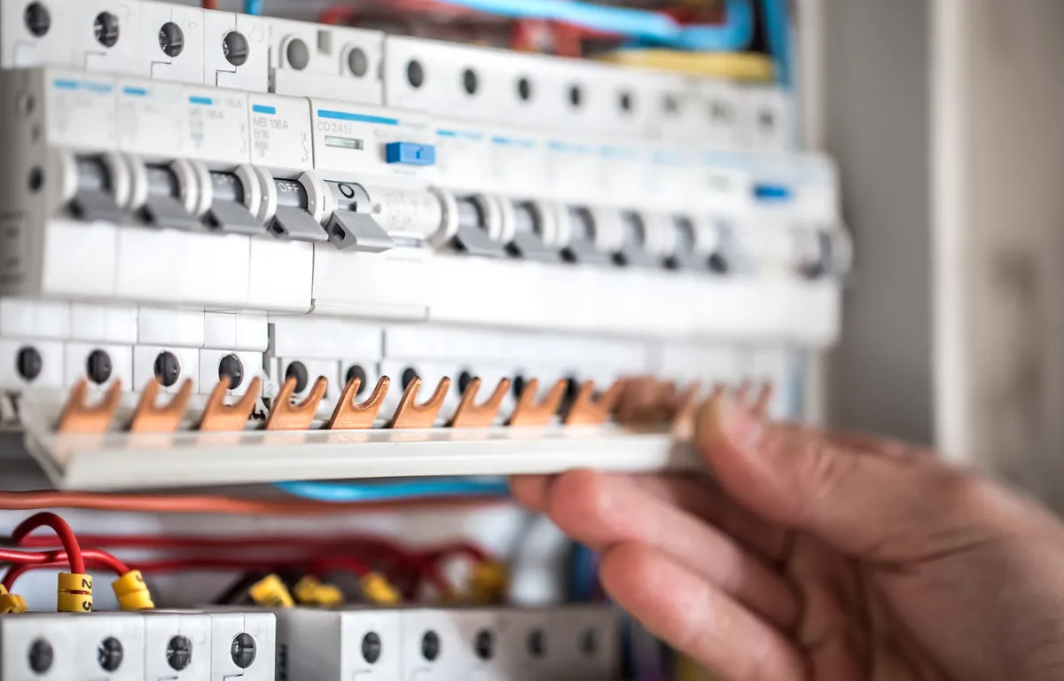 close-up of a hand working on DIN-rail breakers with copper busbar